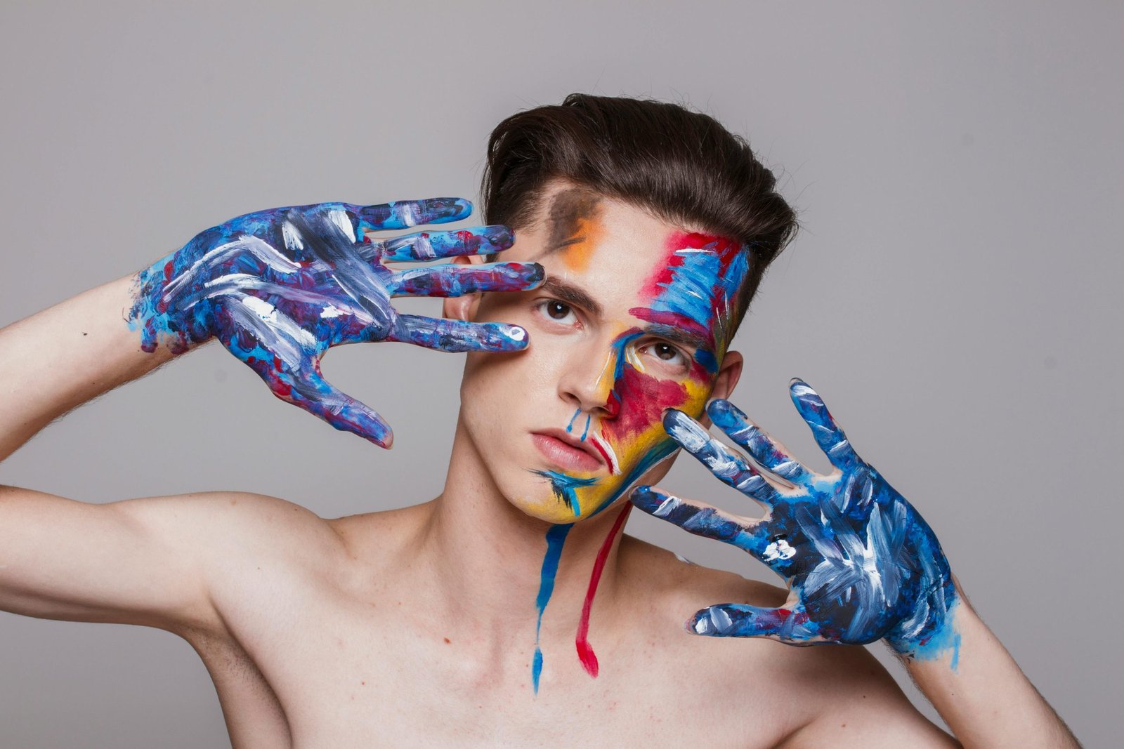 Vibrant artistic portrait of a man with face and hands painted in bright colors, showcasing creativity and expression.